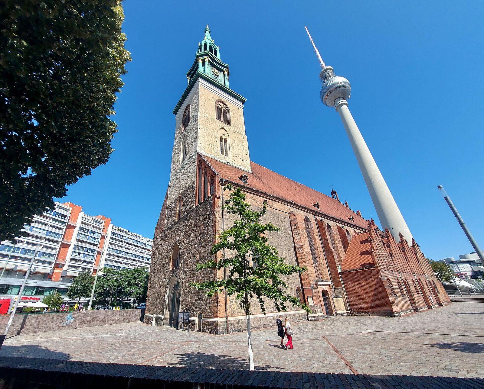 Die Backsteinkirche St. Marien mit ihrem grünen Turmhelm, dahinter ragt der Fernsehturm in den wolkenlosen Himmel