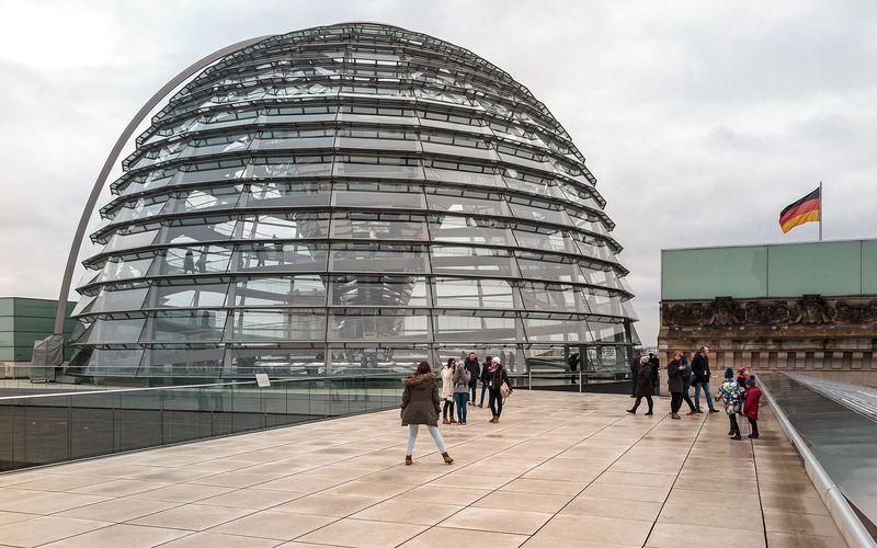 Die gläserne Kuppel auf dem Dach des Reichstagsgebäudes, davor Besucherinnen und Besucher auf der Dachterrasse